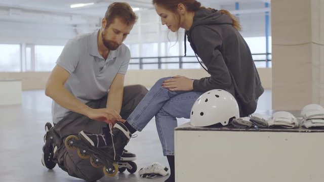 Tilt up of Caucasian bearded man helping young Caucasian woman unlace and take off roller-skates