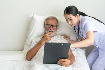 Female nurse showing health check report in chart board to senior man on patient bed - Image