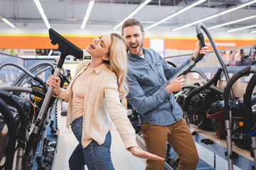 boyfriend playing with vacuum cleaner and girlfriend singing in home appliance store