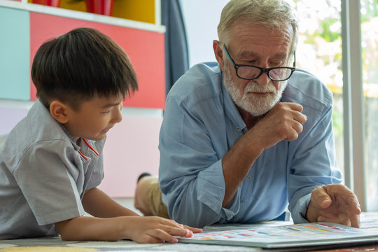 Grandfather and grandson reading a book on living room,  Sernior man teaching grandson for workhome at home, Education concept