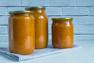 Three transparent glass jars of homemade squash caviar on a white wooden table against a brick wall