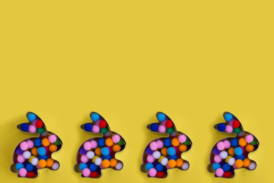 Four abbit bunny shaped forms with colorful balls inside on yellow background. Easter concept. Flat lay with place for text.