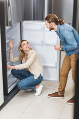 boyfriend talking with smiling girlfriend near fridge in home appliance store