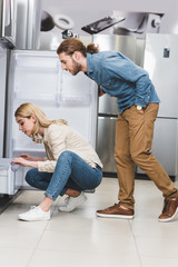 side view of boyfriend and girlfriend looking at fridge in home appliance store