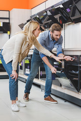 Fototapeta na wymiar consultant use oven and smiling woman pointing with hand in home appliance store