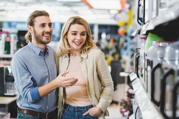 smiling consultant pointing with finger at microwave and talking with woman in home appliance store