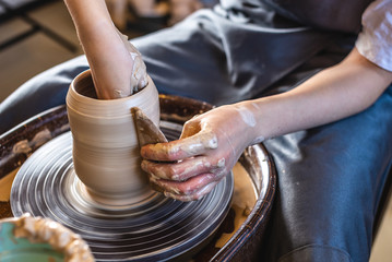 Potter working on a Potter's wheel making a vase. Woman forming the clay with her hands creating jug in a workshop