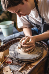 Potter working on a Potter's wheel making a vase. Young woman forming the clay with hands creating jug in a workshop.