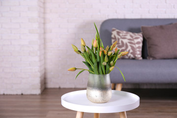 Empty apartment with minimal loft style interior, wooden floor and glass vase with bouquet of tulips on foreground and blank wall with a lot of copy space for text on background. Close up.