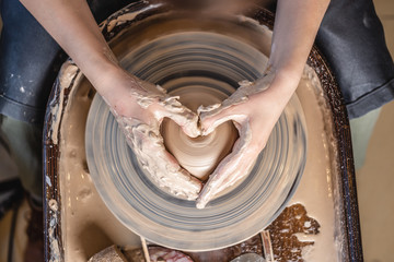 Potter working with clay on a Potter's wheel. Women's hands show a heart sign. Concept of love for pottery art - obrazy, fototapety, plakaty