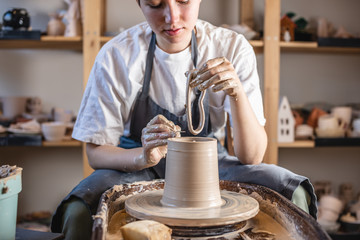 Potter working on a Potter's wheel making a vase. Young woman forming the clay with hands creating jug in a workshop.