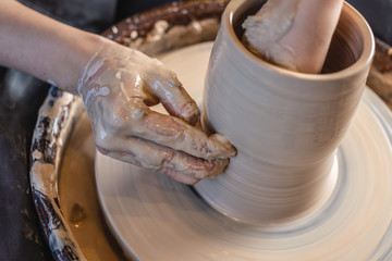 Woman potter working on Potter's wheel making a vase. Master forming the clay with her hands creating jug in a workshop