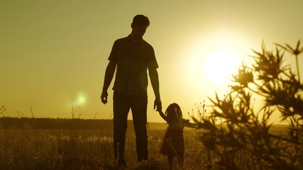 child holds father's hand. dad and baby are resting in park. child plays with his father. little daughter and dad walk around field holding hands. family walks in evening out of town.
