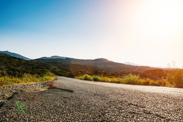 Empty long mountain road to the horizon on a sunny summer day at bright sunset