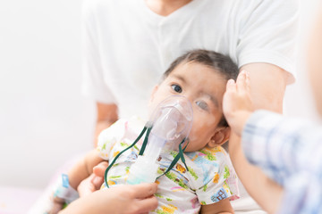 Asian little baby boy is is treated respiratory problem with vapor nebulizer and sister's hand is...