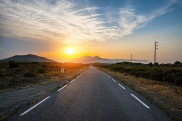 Empty long mountain road to the horizon on a sunny summer day at bright sunset