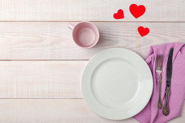 Valentines day romantic table setting, red tape, paper hearts tea cup, plate, silverware, pink napkin on white wooden background. Copyspace, empty place for text. Top view, flat lay, horizontal.