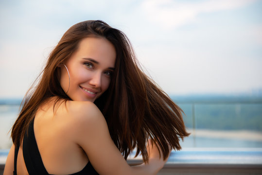 Fashion model wearing black elegant dress posing evening outdoor at the bank of Dniper river in Kyiv, Ukraine. Young beautiful brunette caucasian woman walking summer streets. Beautiful girl