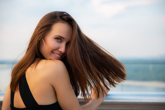 Fashion model wearing black elegant dress posing evening outdoor at the bank of Dniper river in Kyiv, Ukraine. Young beautiful brunette caucasian woman walking summer streets. Beautiful girl