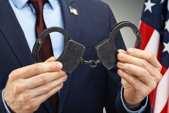 Male in suit holding metal handcuffs with USA flag on background - close up studio shot