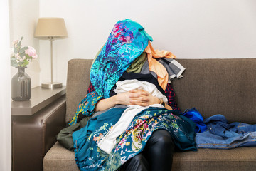 greedy shopping obsessed woman sitting on couch with clothes heap on her