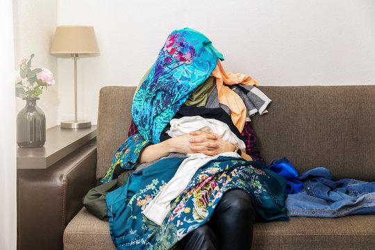 Greedy Shopping Obsessed Woman Sitting On Couch With Clothes Heap On Her