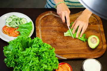 Woman cuts the salad on wooden cutting board. flat lay