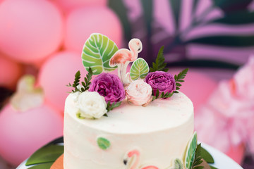 Pink cake with flamingos for the holiday. Cake with a variety of decorations, palm leaves and fresh flowers