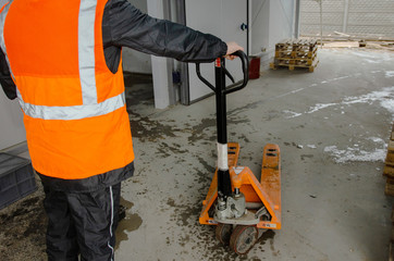  warehouse worker in workwear and safety helmet is working with hand pallet truck or pallet jack and shipments in distribution warehouse