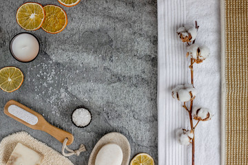 Soap, scrubber, pumice and sea salt on a grey stone table, with orange slices and a cotton branch...