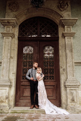 stylish young man with beard and woman in luxury long dress on wedding day near the castle. Romantic love in vintage atmosphere street.