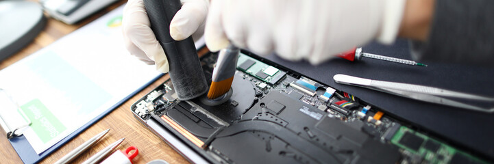 Close-up of male technician hands using vacuum cleaner and brush to sweep dirt from pc. Workplace of IT specialist with tools and instruments on table