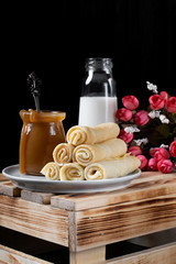 Obraz na płótnie Canvas Stack of rolled crepes on the ceramic plate, a glass jar of salted caramel and a bottle of milk