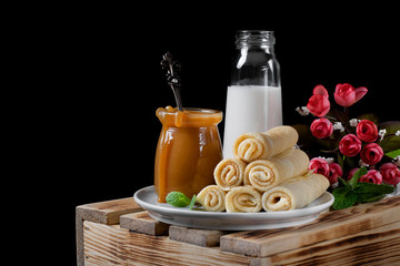 Obraz na płótnie Canvas Salted caramel in a glass jar, a stack of crepes on the ceramic plate and a bottle of milk