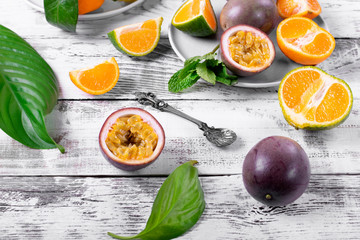 Passion fruit and tangerines on the white wooden table. Whole and sliced tropical fruits