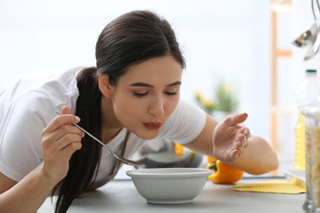 Young woman eating tasty vegetable soup at countertop in kitchen
