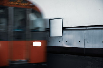 Blurred movement of a red metro train arriving at station with empty billboard space