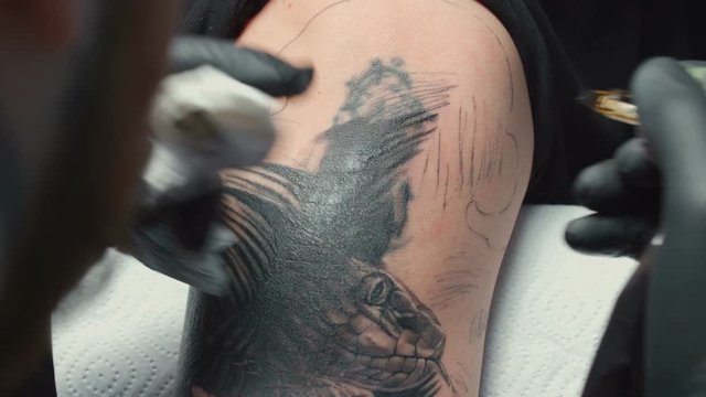 Shooting of man tattooist getting tattoo of snake for woman