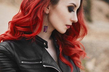 Fashionable close-up portrait of a model girl with red hair and trendy makeup in a leather jacket....