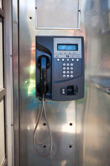 Public phone in steel booth with physical land line communication, push button phone