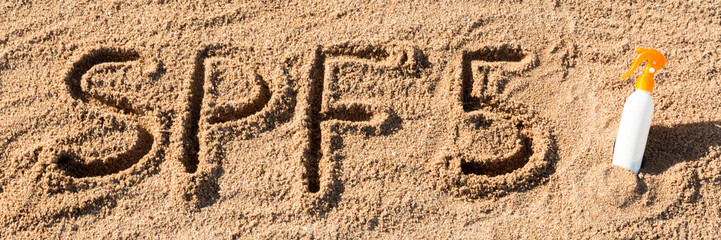 Sun protect factor five. SPF 5 word written on the sand and white bottle with suntan cream. Skin care concept background