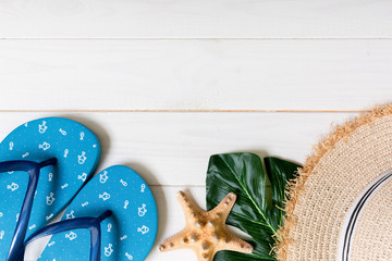 Straw hat, green leaf, blue flip flops and starfish On a white wooden background. top view summer...