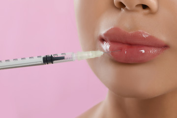 Young woman getting lips injection on pink background, closeup