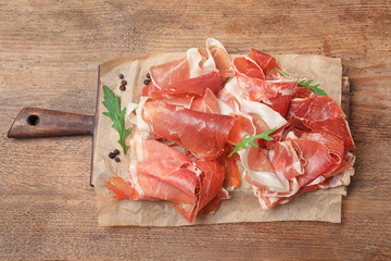 Pile of tasty prosciutto on wooden table, top view