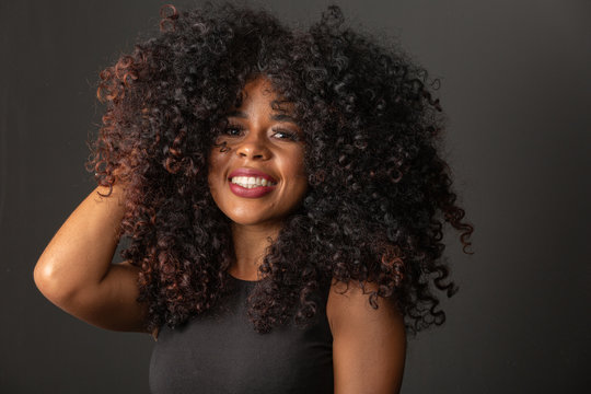 Young afro-american woman with curly hair looking at camera and smiling. Cute afro girl with curly hair smiling looking at camera.