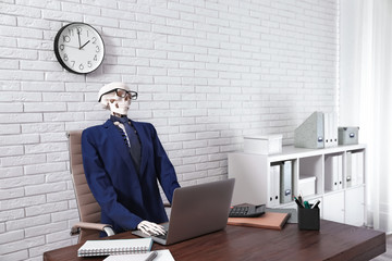Human skeleton in suit using laptop at table in office
