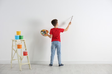 Little child painting on blank white wall indoors