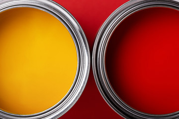 Cans of yellow and red paint on red background. Top view, minimal styled.