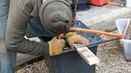 Man using hacksaw to cut piece of wood