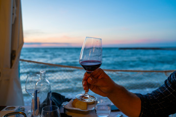 Male hand holding glass with wine on blurred natural sea sunrise background.